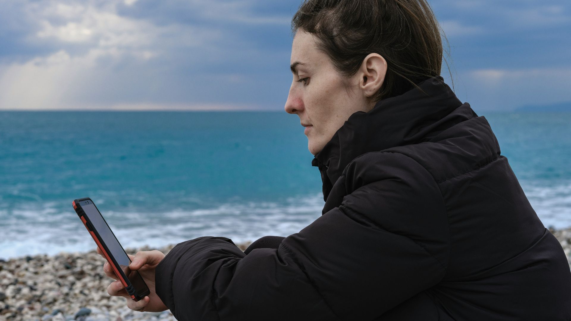 a woman sitting on the beach looking at her cell phone