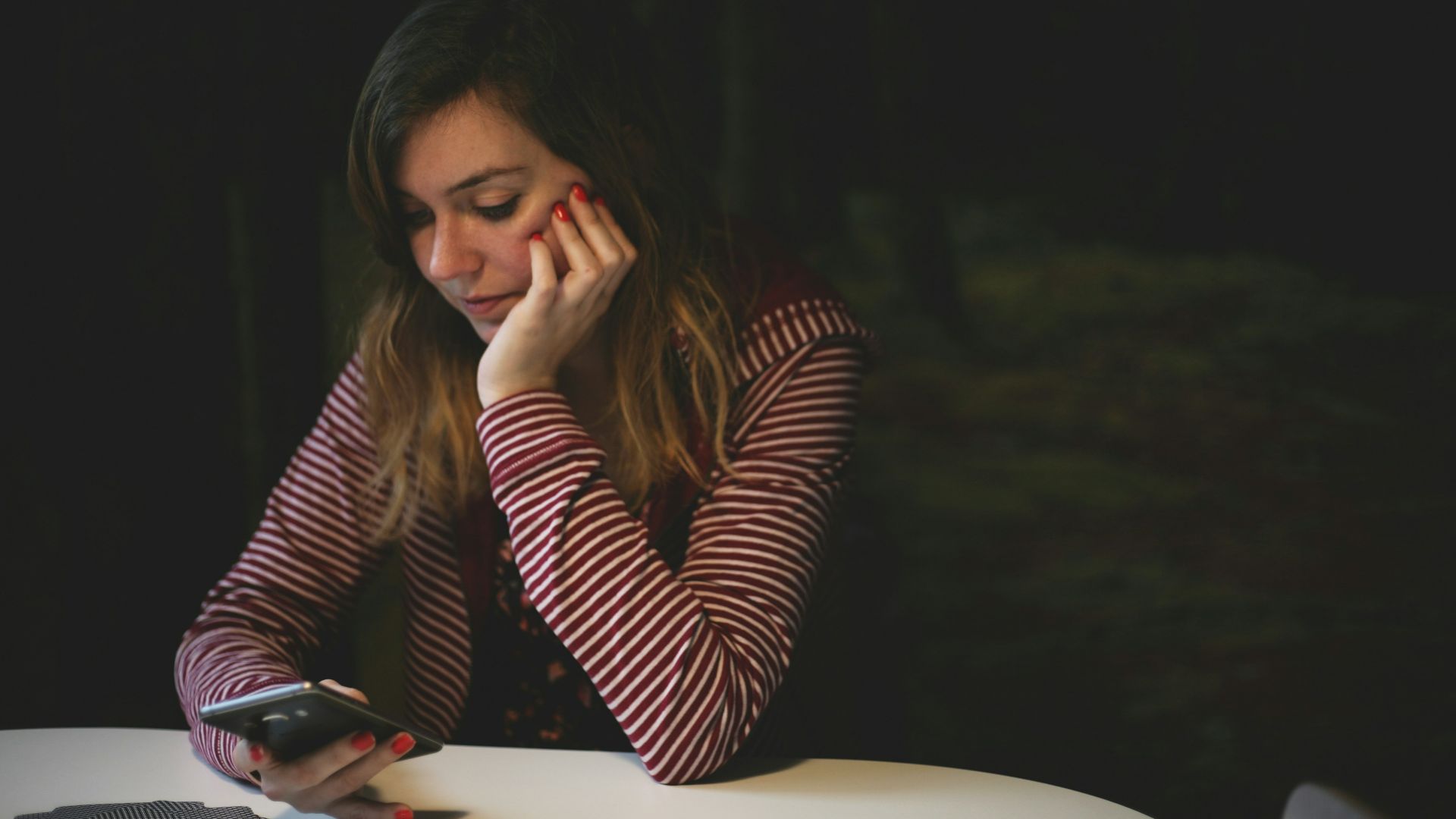 woman leaning on white wooden table while holding black Android smartphone