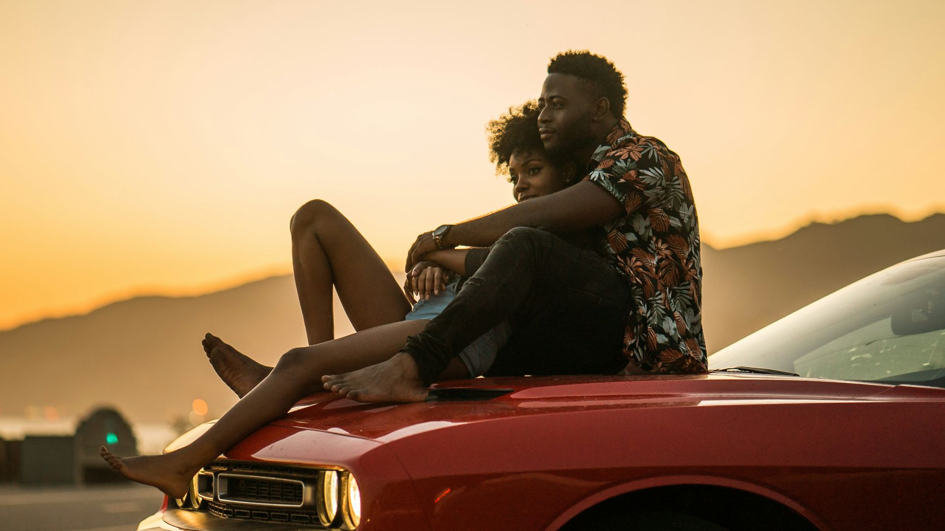woman in black and white floral dress sitting on red car hood during daytime
