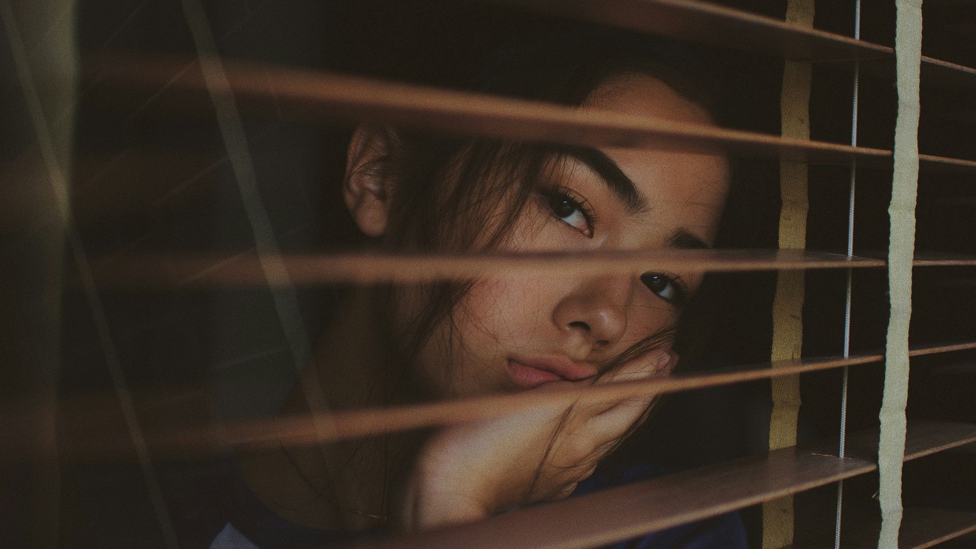 a woman looking out of a window with blinds