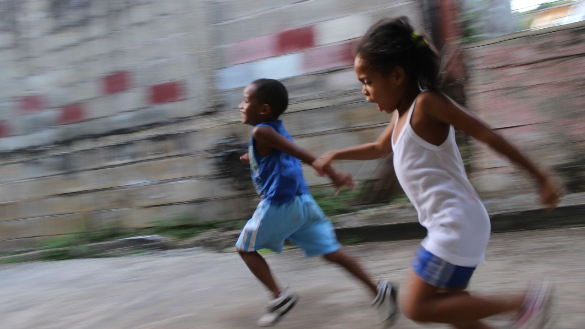 two girl and boy running beside gray wall