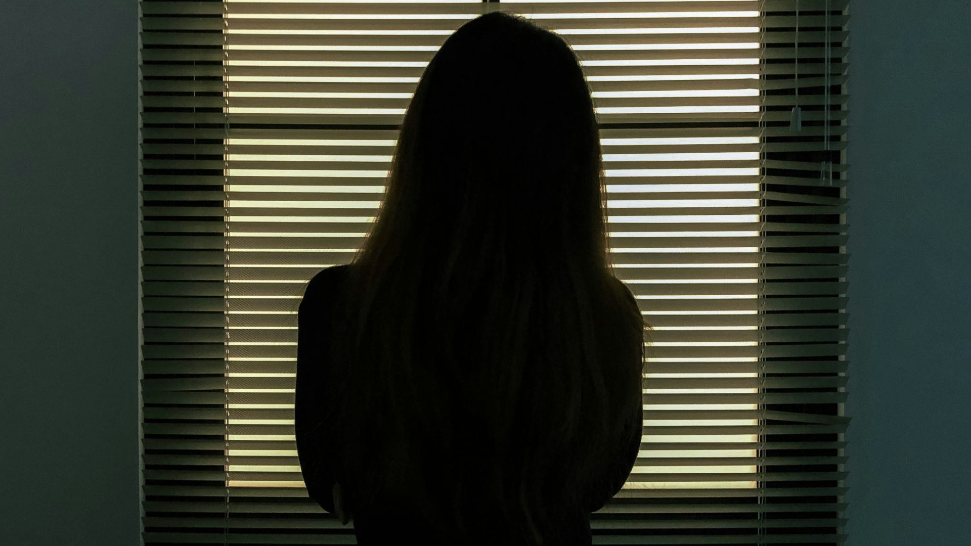 woman in black shirt standing near window blinds