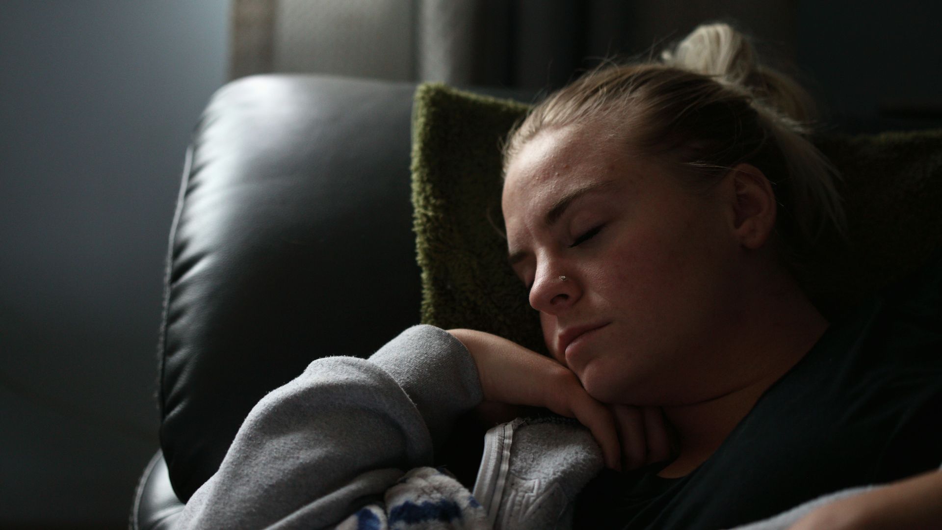 boy in gray hoodie lying on black leather couch
