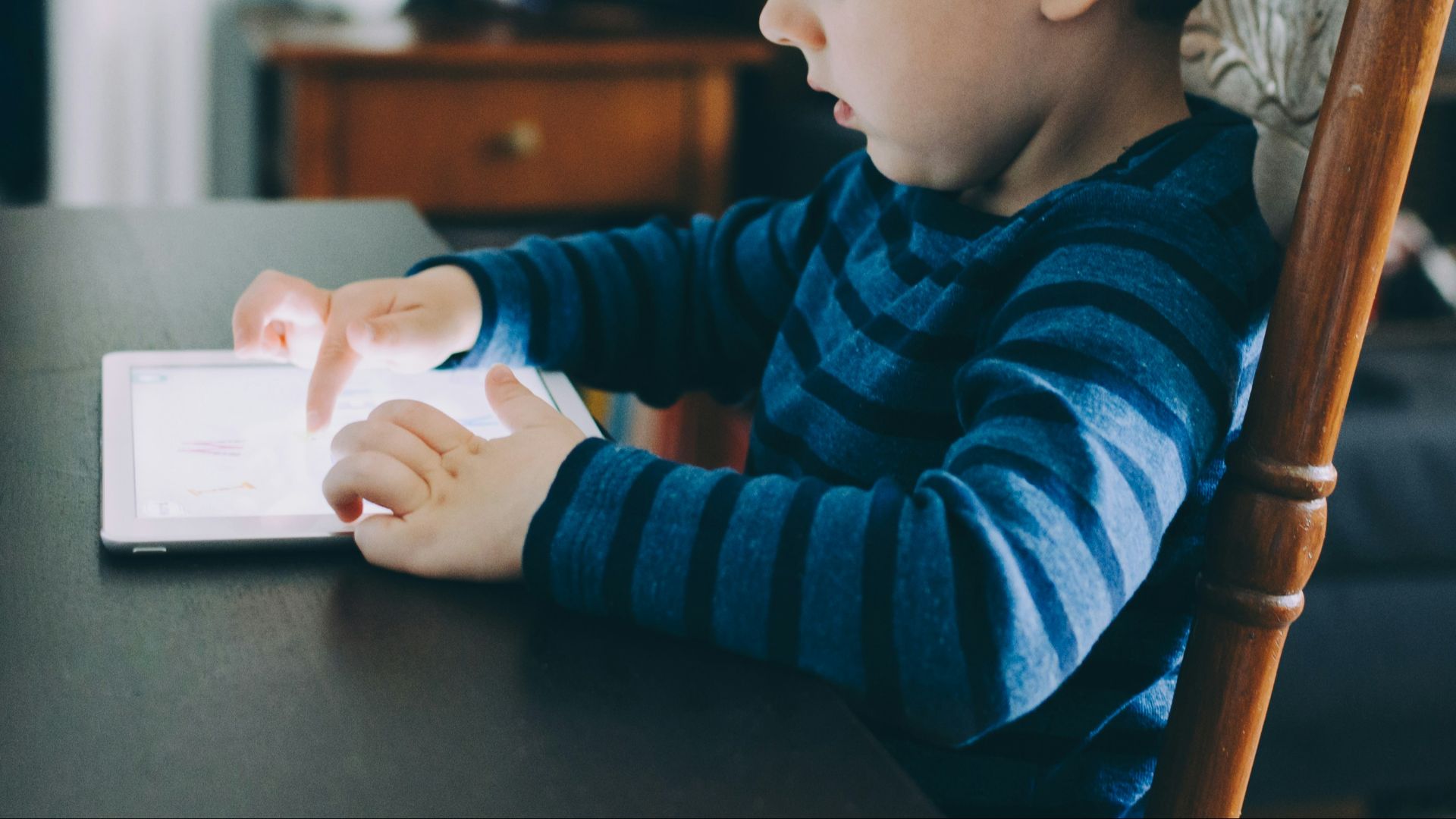 boy sitting on chair beside table using tablet computer