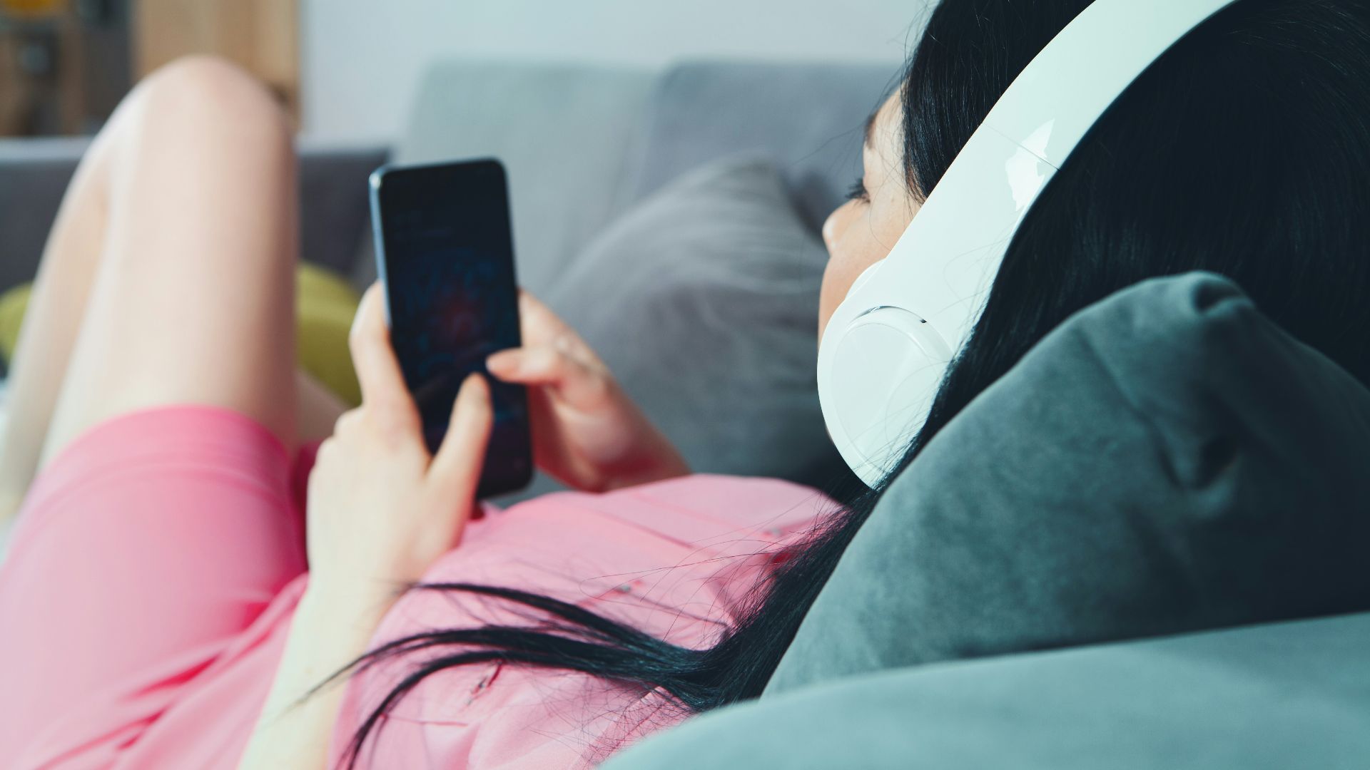 woman in pink shirt lying on bed holding smartphone