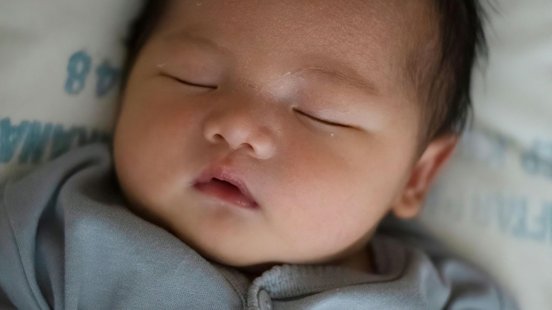 baby in gray onesie lying on bed