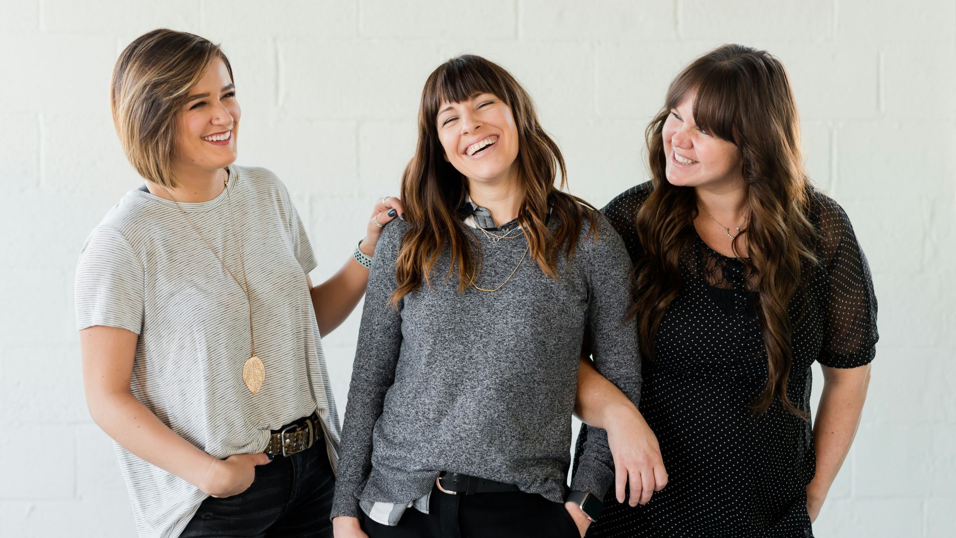 3 women smiling and standing beside white wall