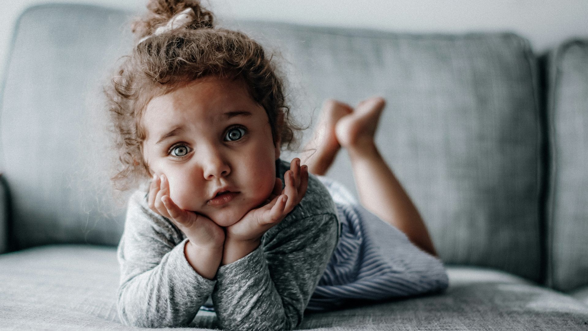 girl in gray long sleeve shirt lying on gray textile