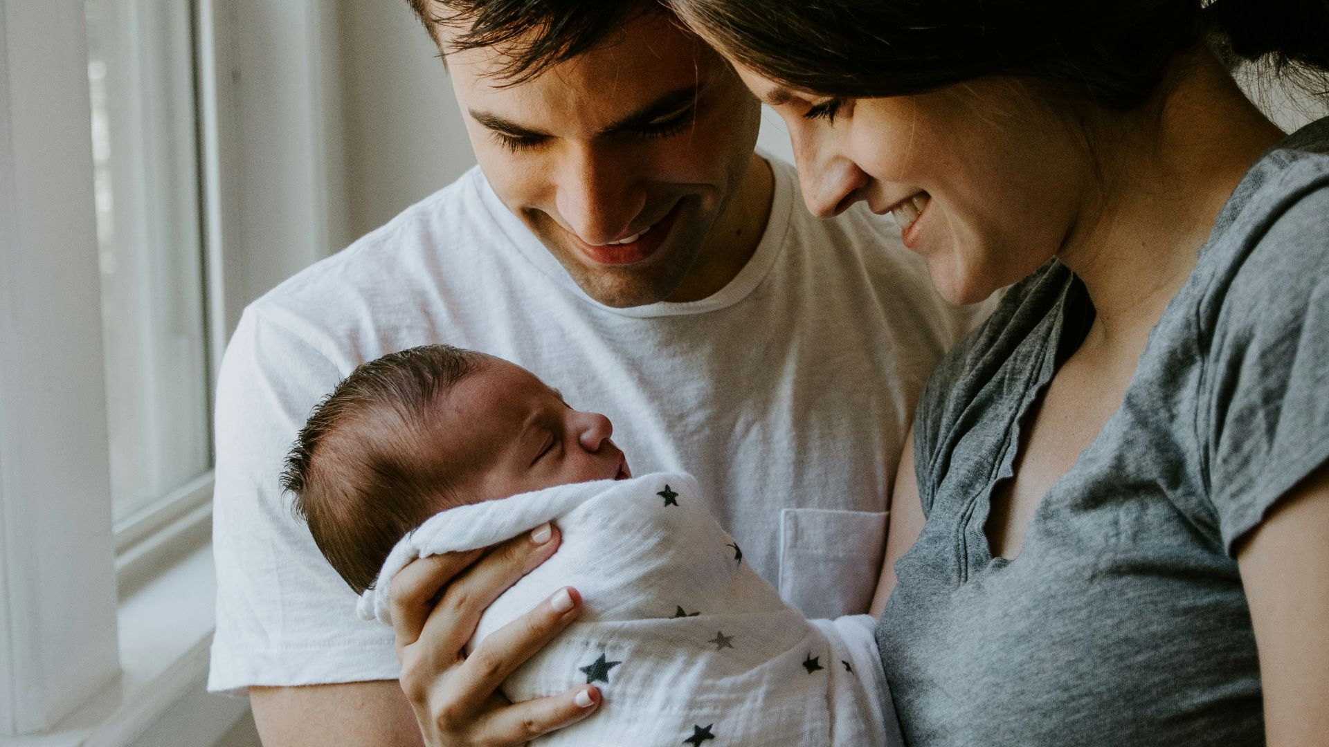 woman holding baby beside man smiling