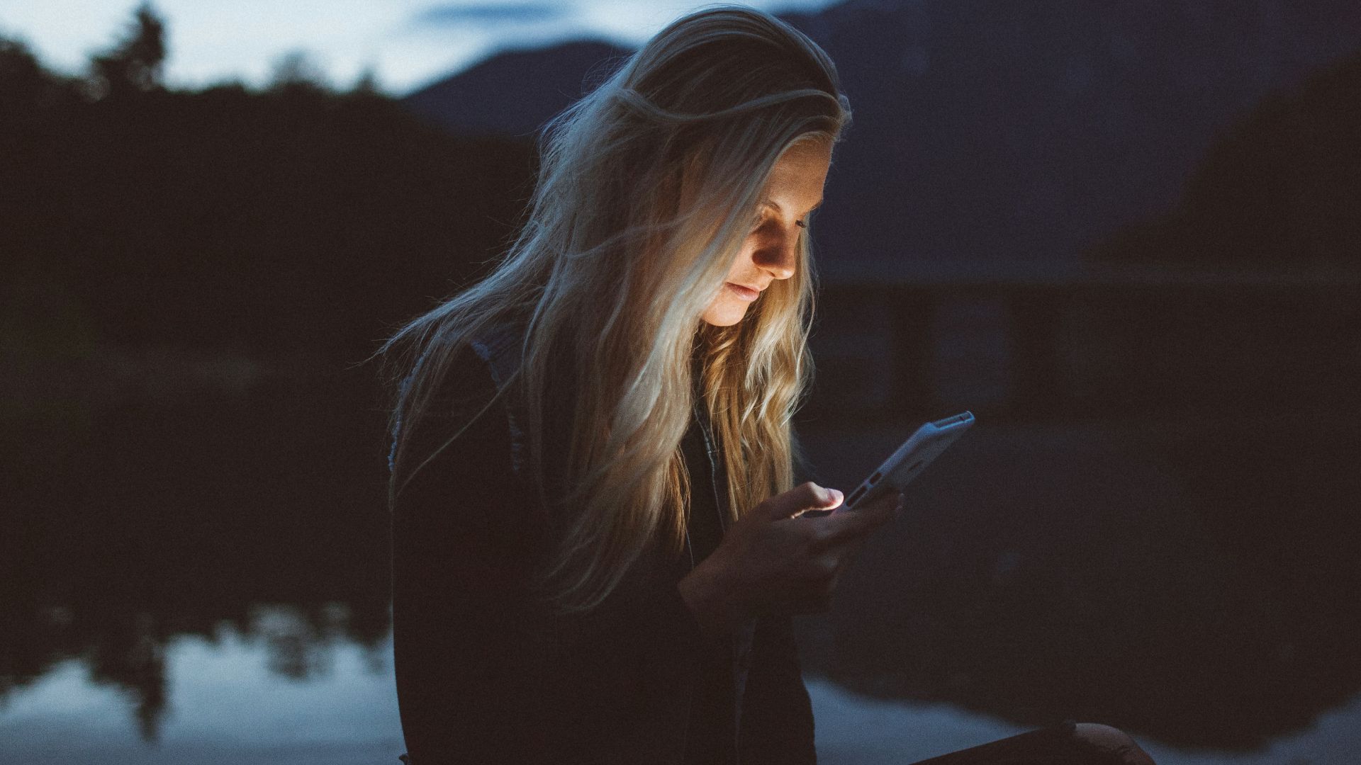 woman looking at phone beside body of water