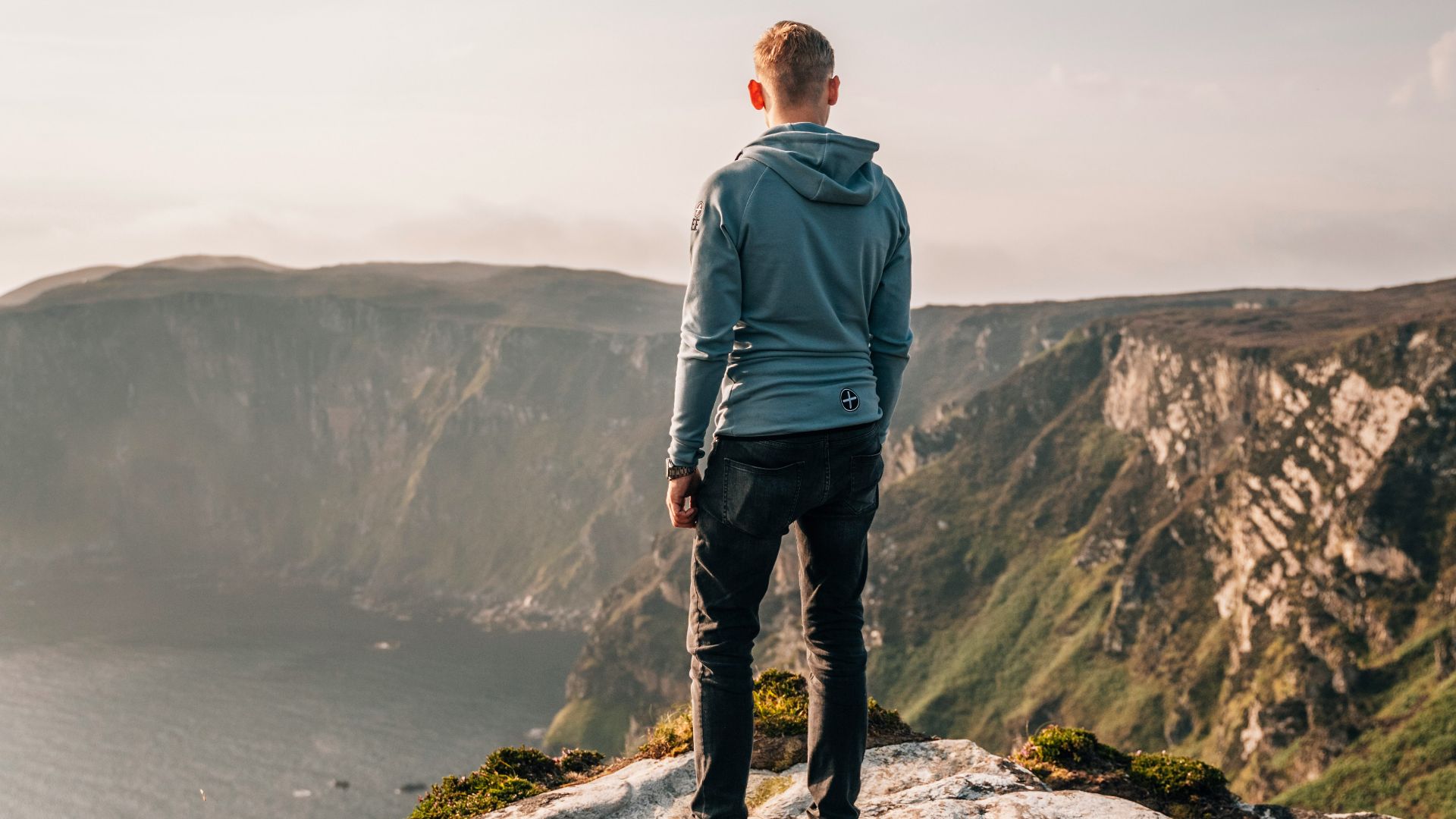 man in blue jacket standing on rock formation near body of water during daytime