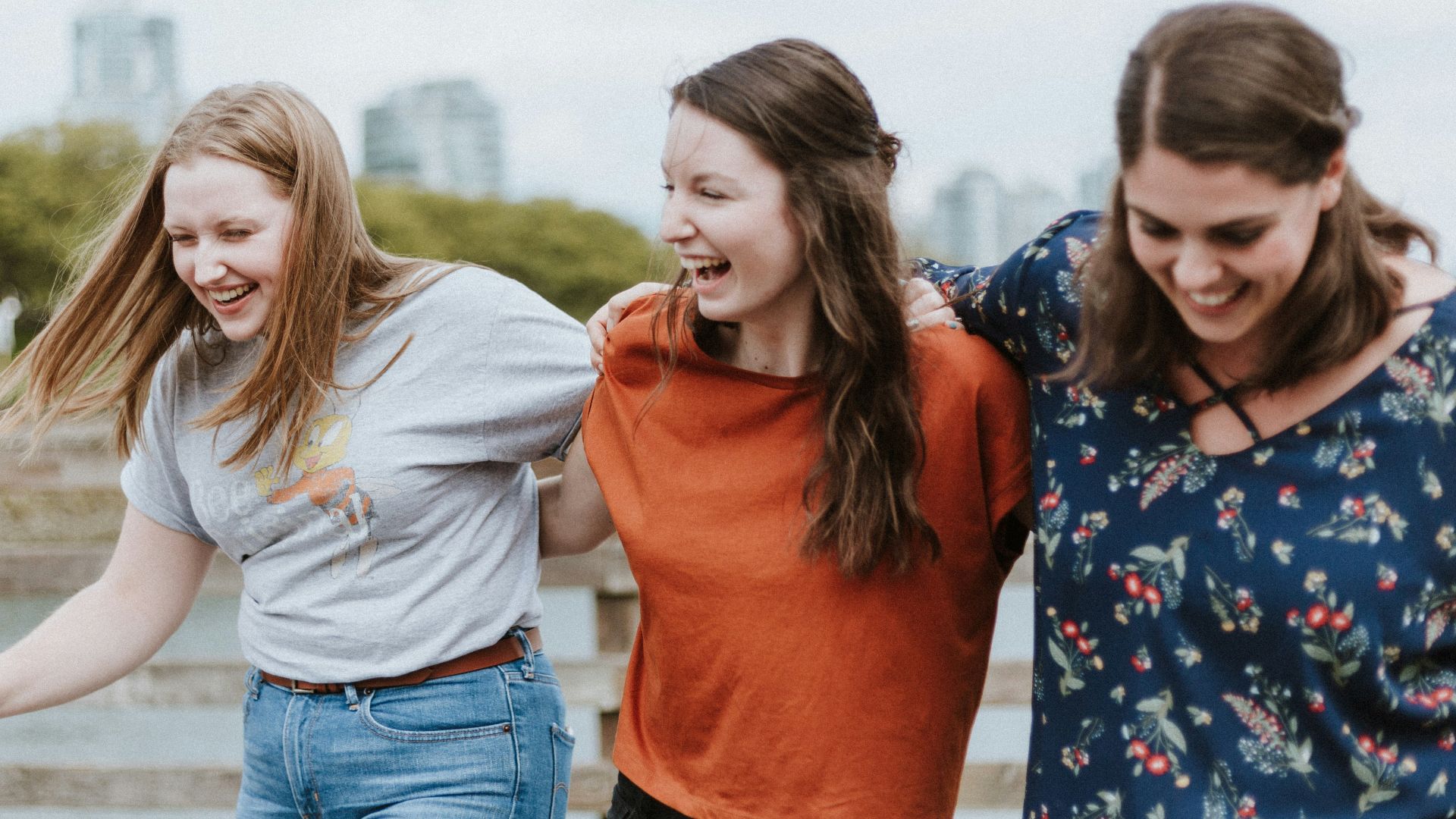 three women walking on brown wooden dock near high rise building during daytime