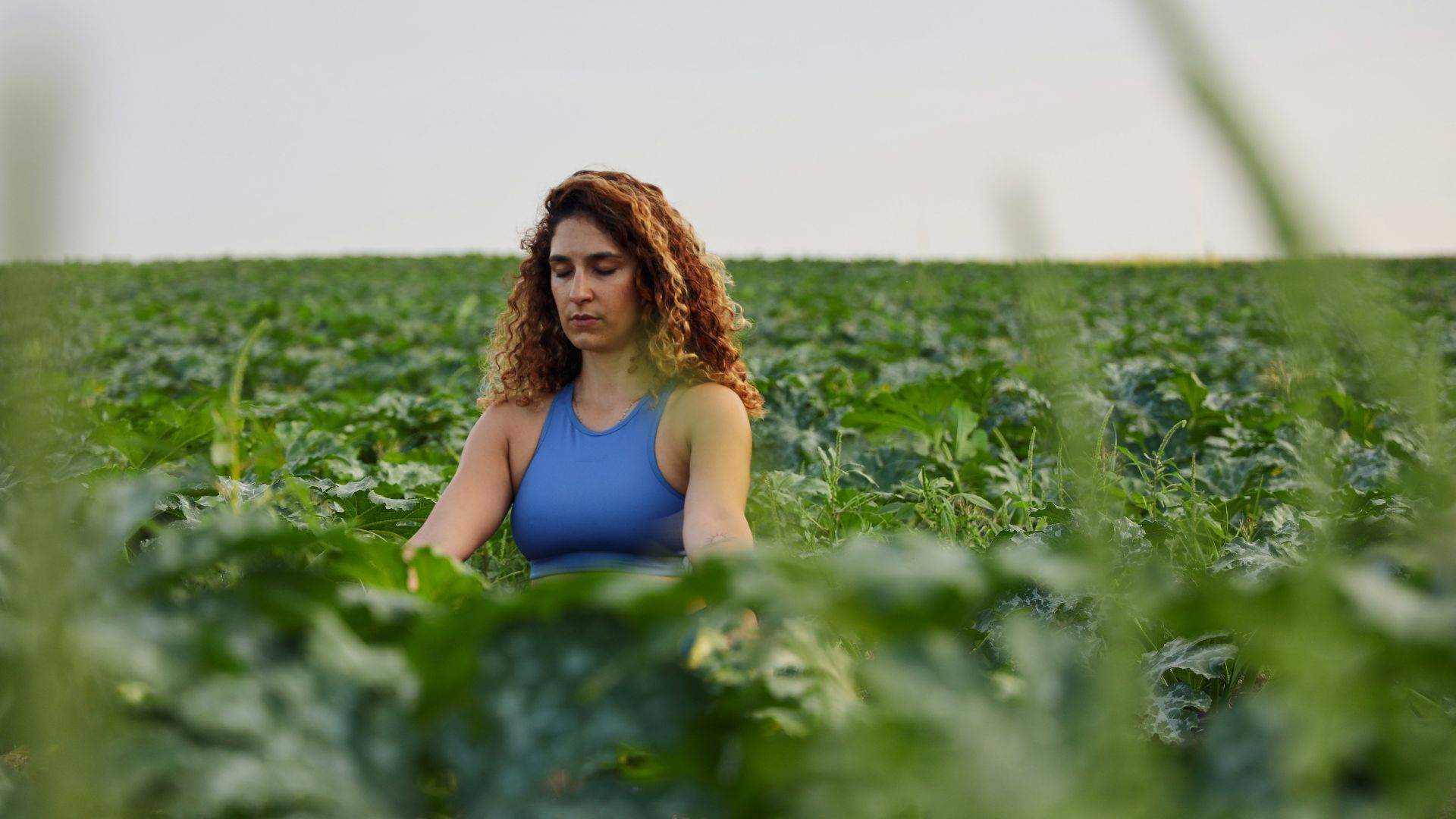 selective focus photography of woman meditating while sitting on ground surrounded by plants during daytime
