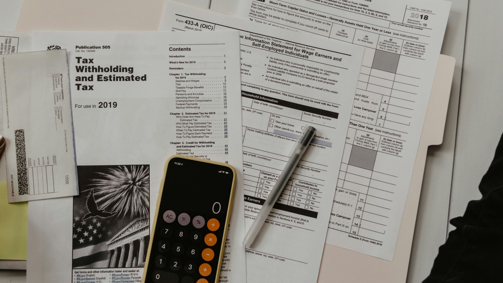 person holding paper near pen and calculator
