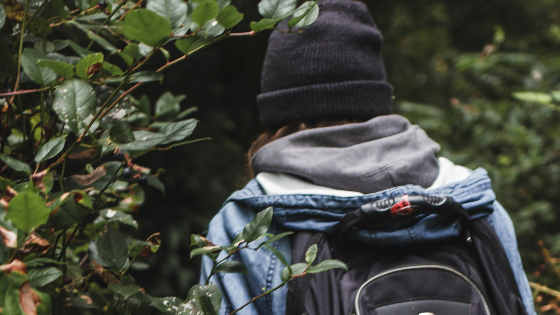 person in green jacket and black backpack standing in front of green plants