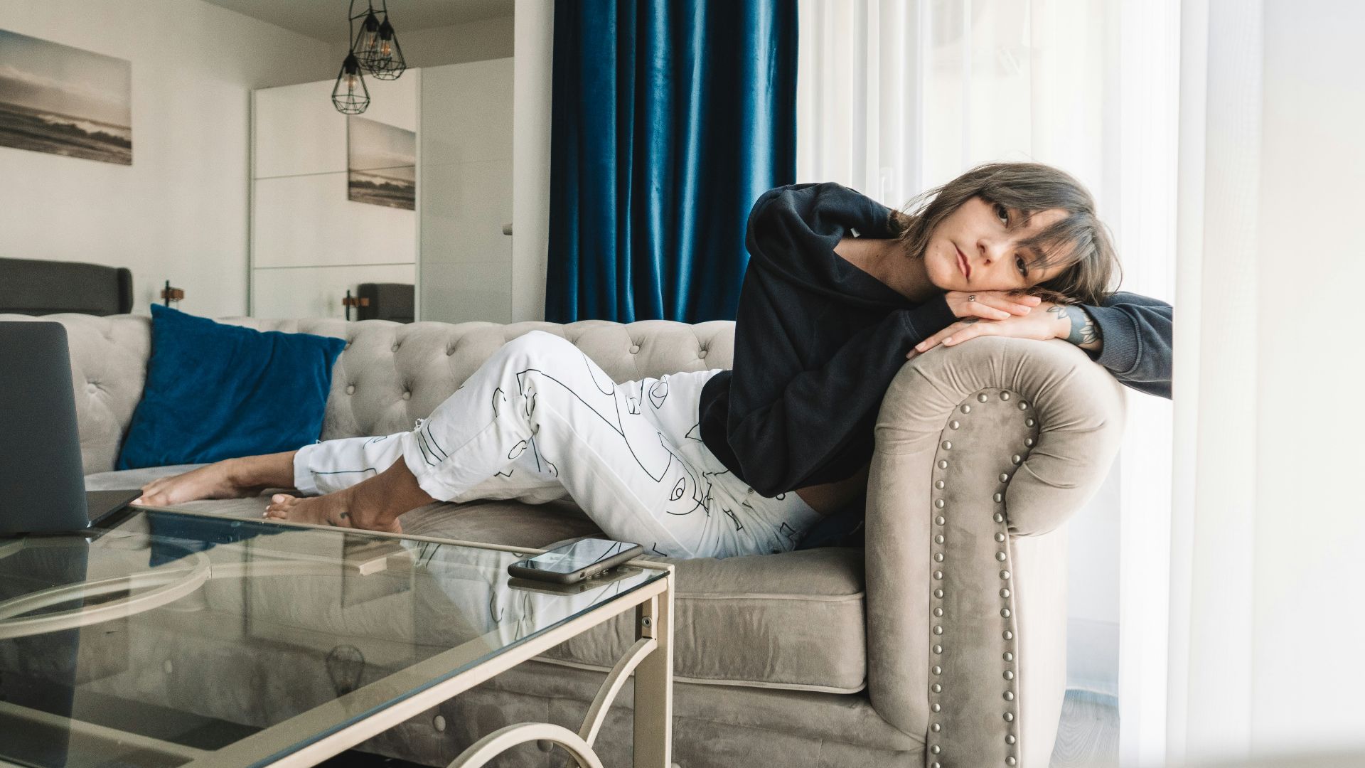 woman in gray sweater and blue denim jeans sitting on gray couch