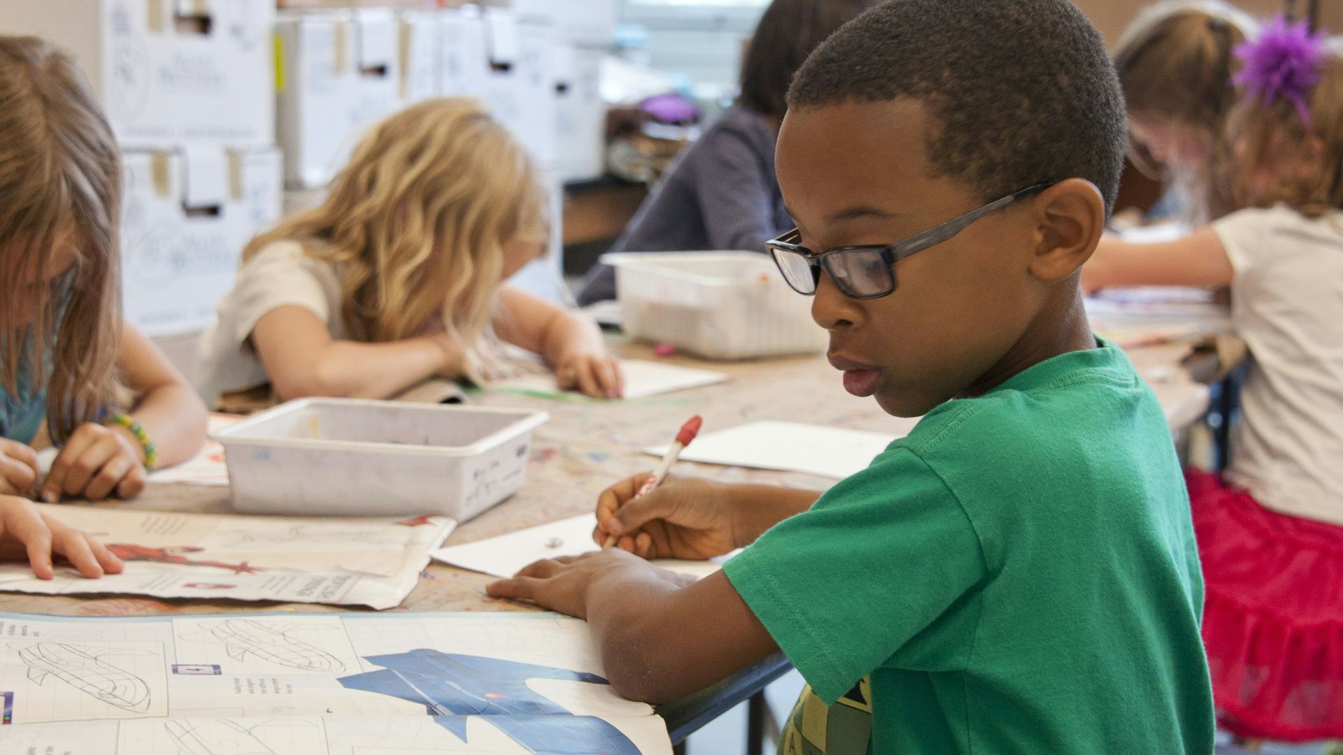 boy in green sweater writing on white paper