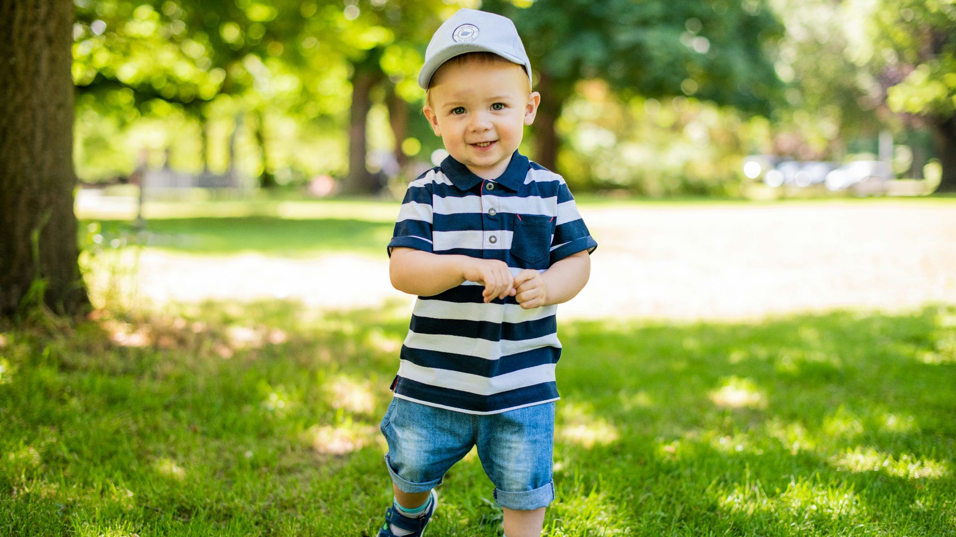 boy in black and white stripe polo shirt and blue denim shorts standing on green grass