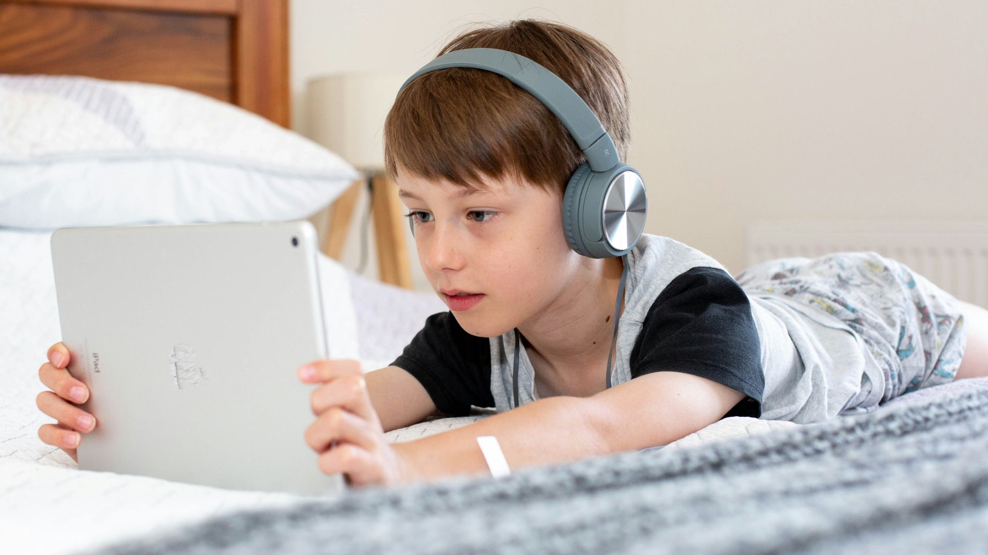 boy in blue shirt wearing headphones lying on bed