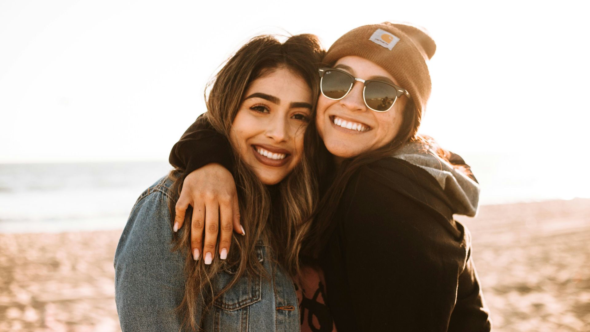 woman hugging other woman while smiling at beach