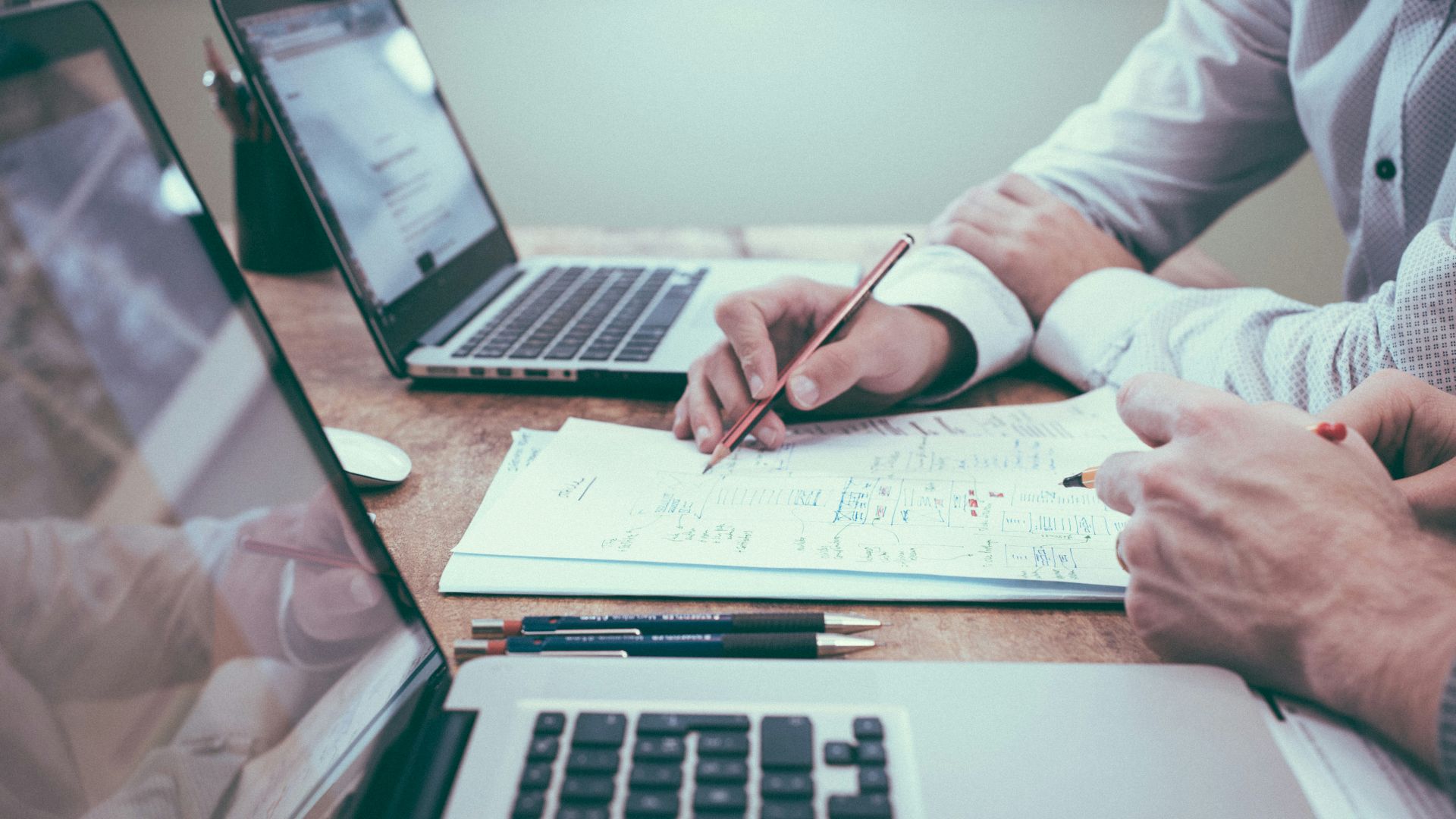 person holding pencil near laptop computer