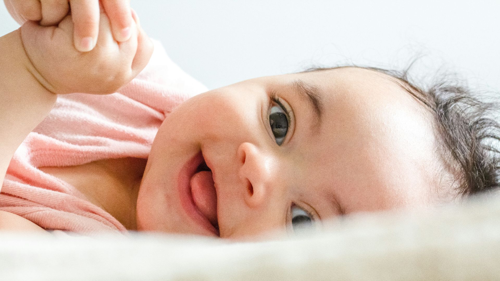 baby in pink shirt lying on white textile