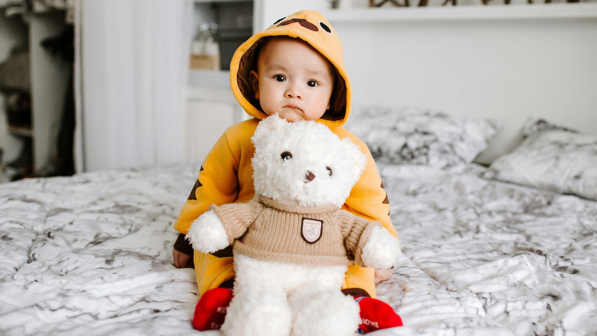 toddler sitting on bed beside white bear plush toy