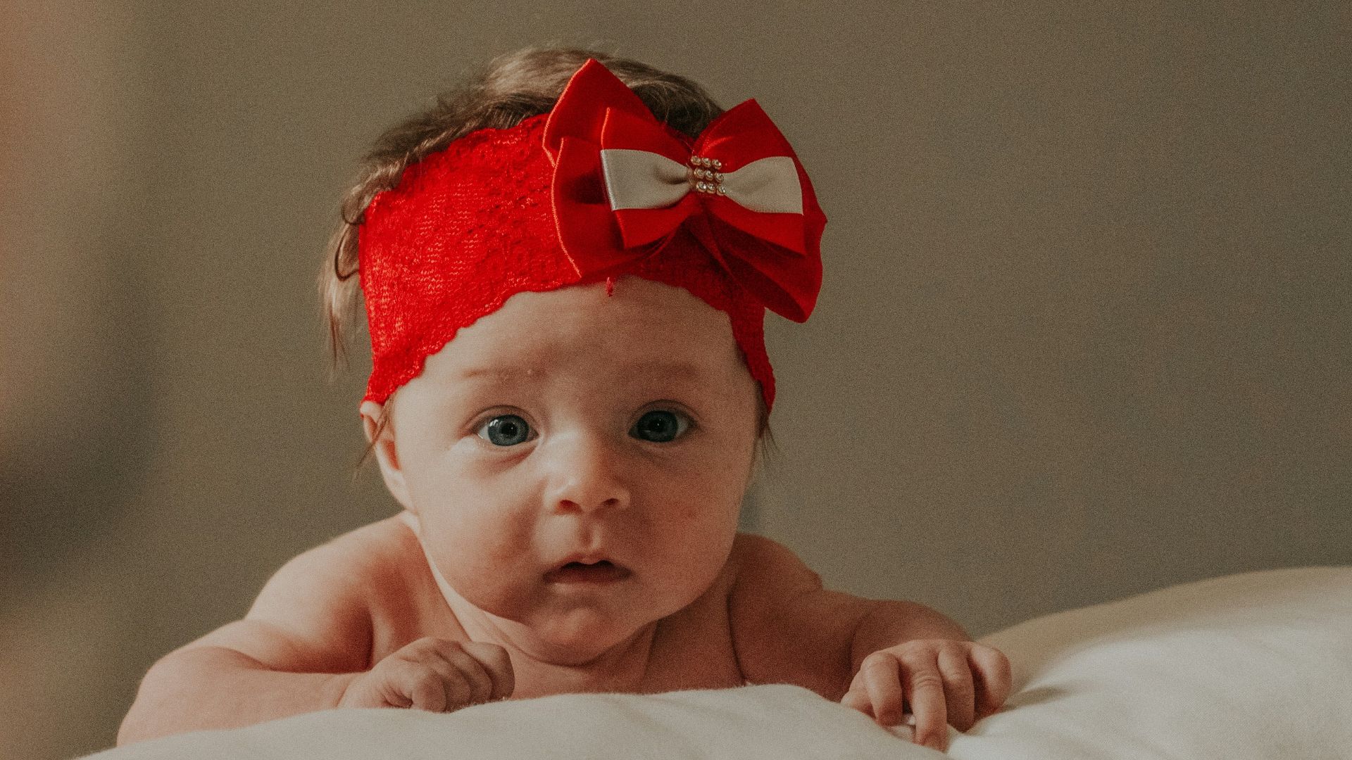 baby in red headband lying on bed