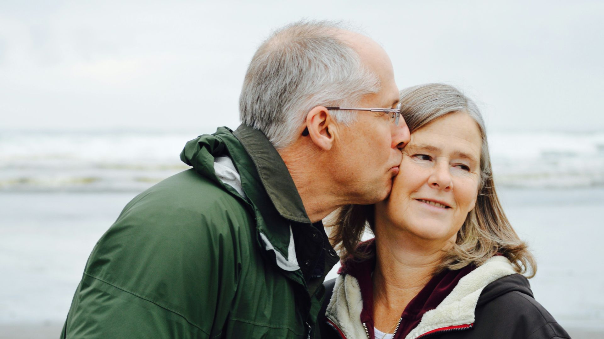man kissing woman on check beside body of water