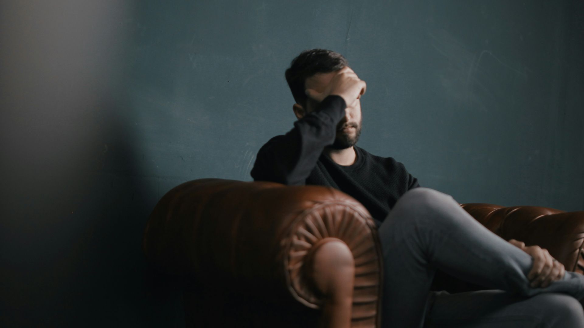 a man holds his head while sitting on a sofa