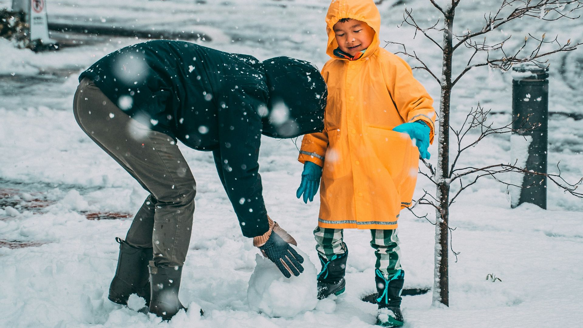 child in yellow jacket and black pants playing on snow covered ground during daytime