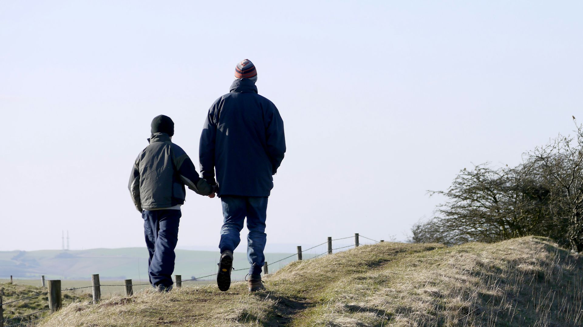 man and boy walking on grass near fence