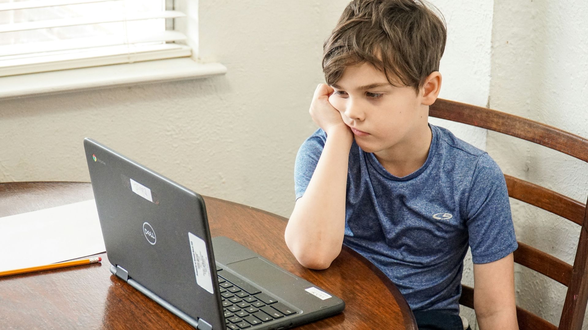 boy in blue crew neck t-shirt using macbook pro on brown wooden table