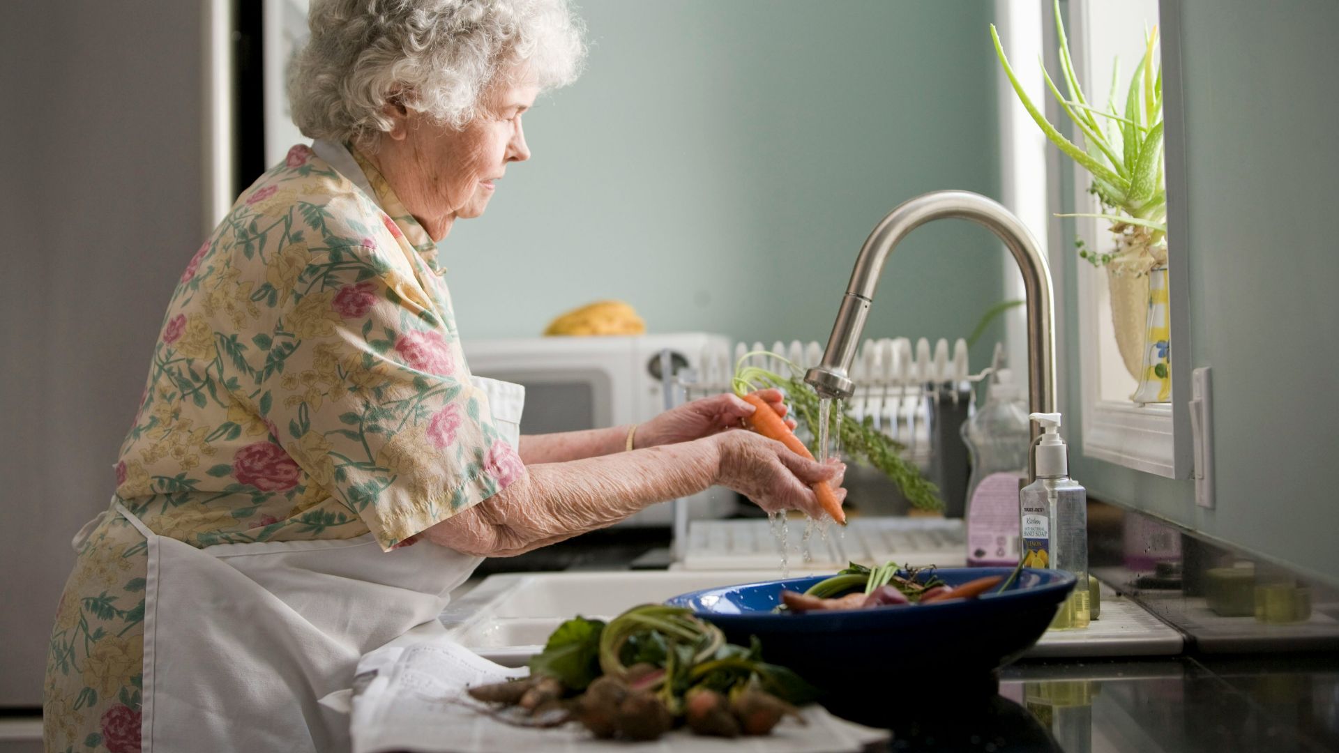 woman wearing yellow and pink floral dress wahing carrots