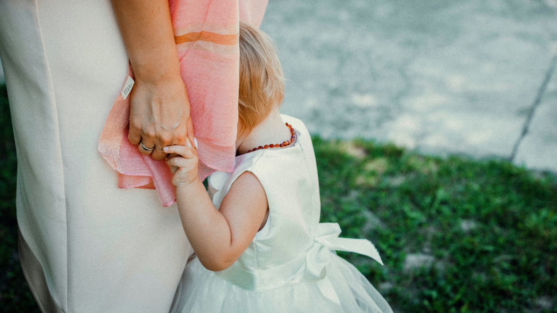a little girl in a white dress is holding her mother's hand