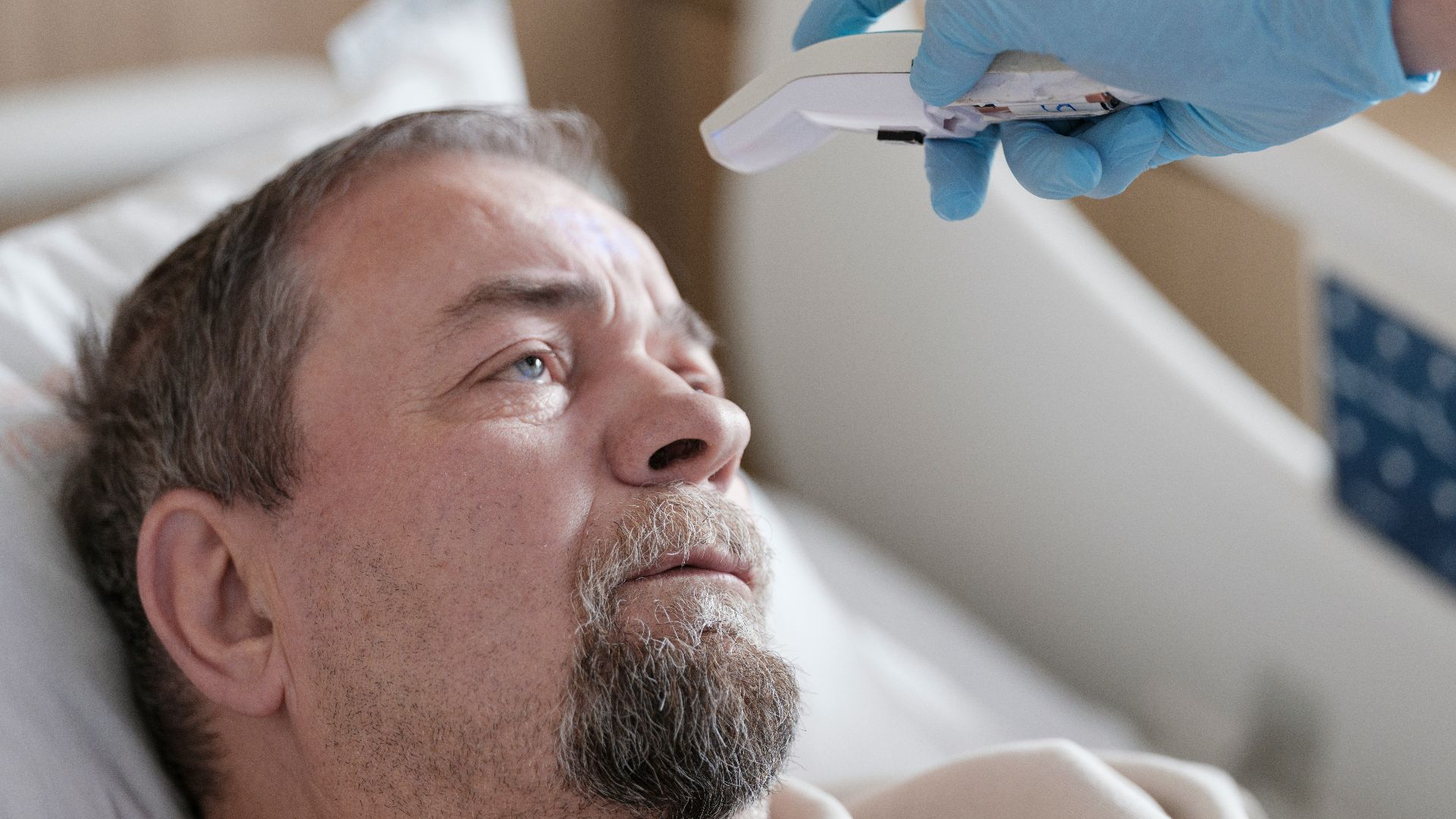 a man laying in a hospital bed with a thermometer in his hand