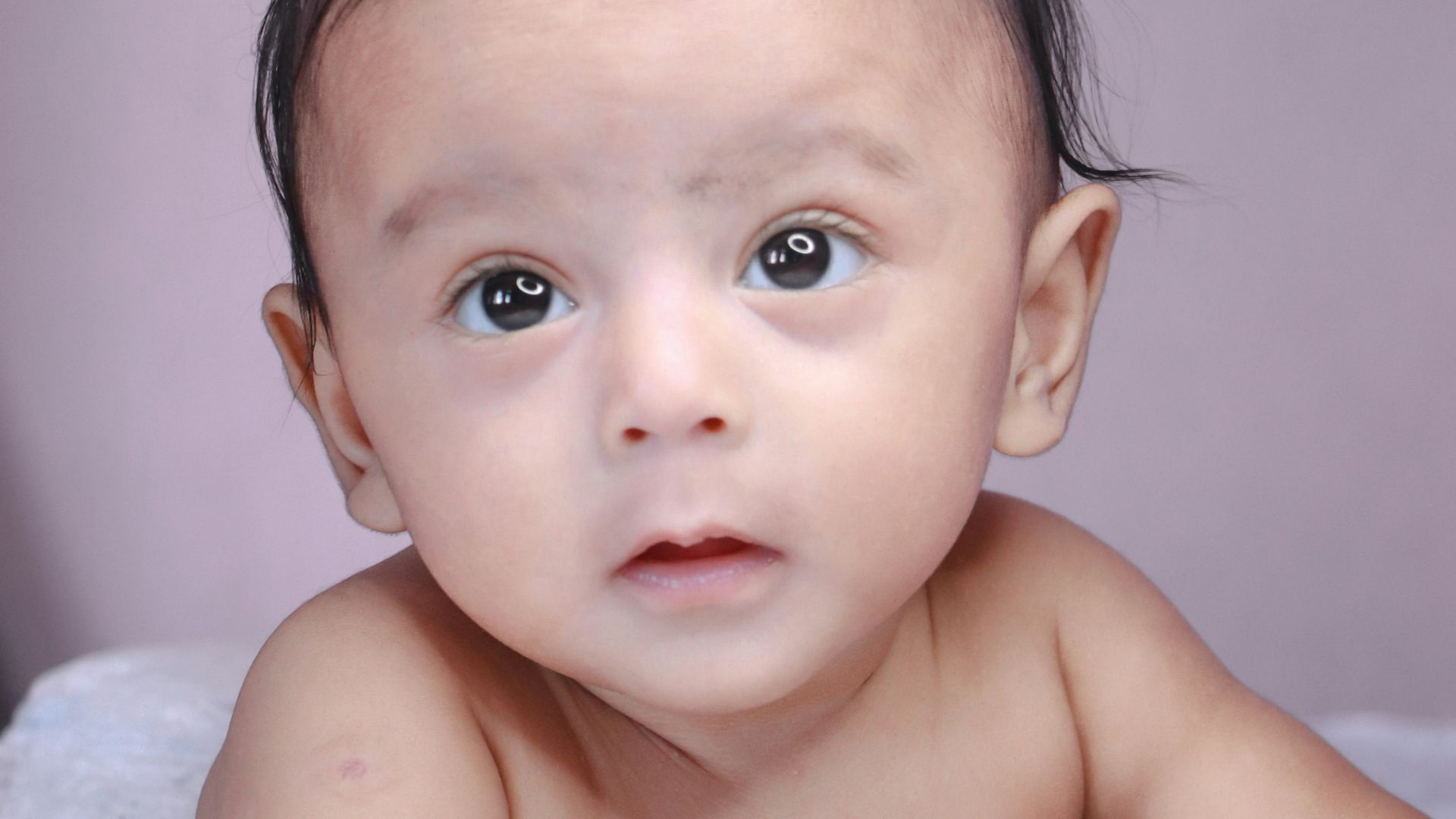 topless baby lying on white textile