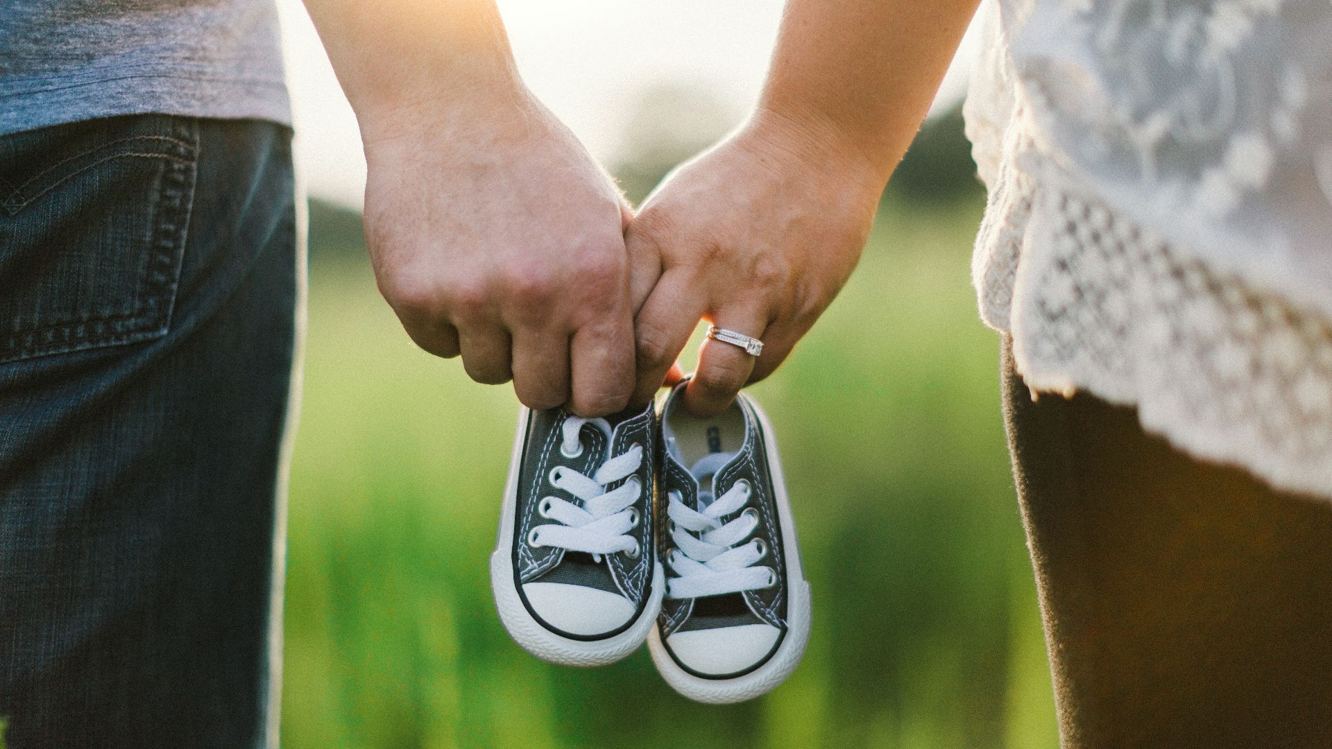 woman and man holding black crib shoes standing near green grass during daytime