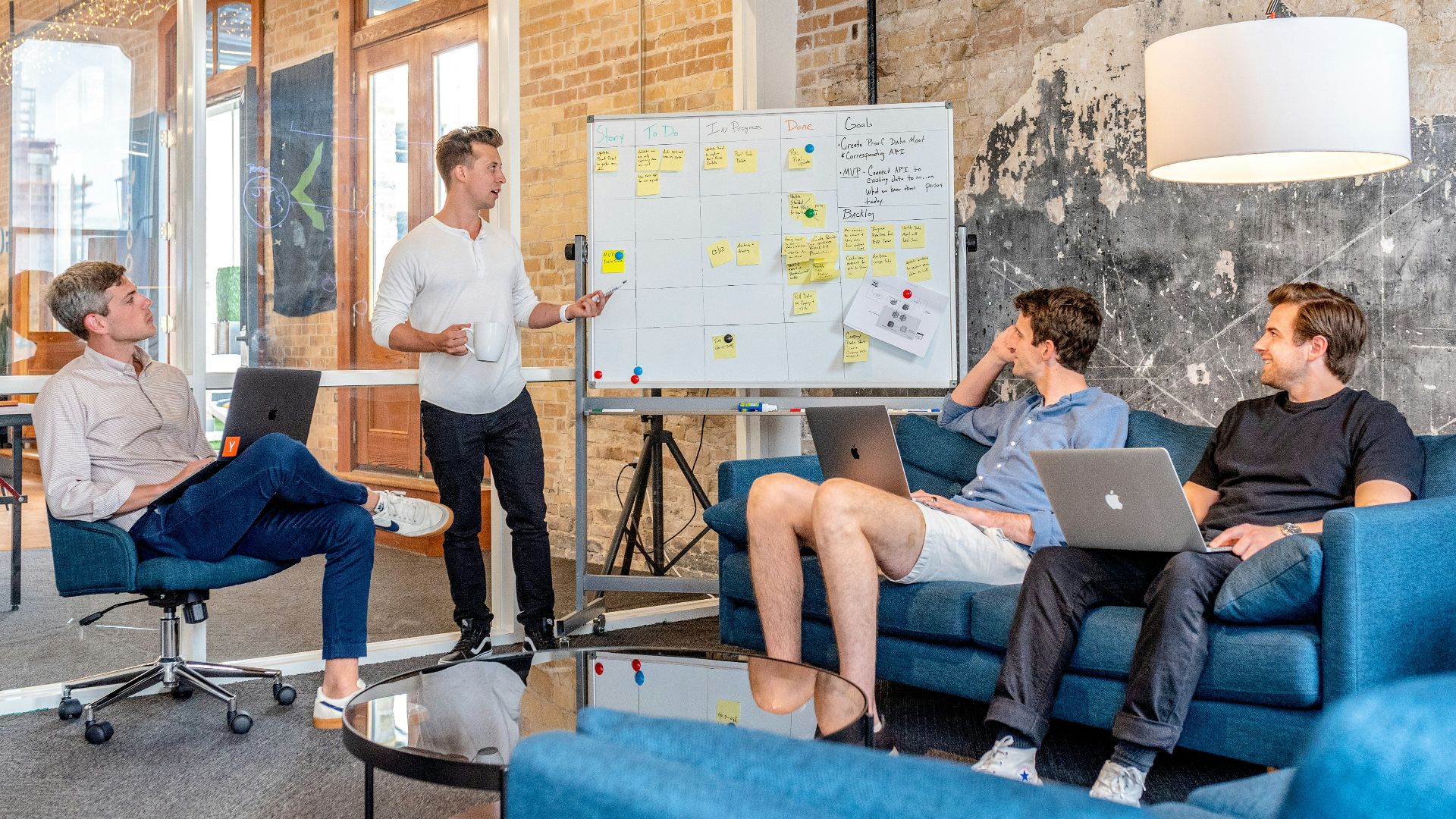 three men sitting while using laptops and watching man beside whiteboard