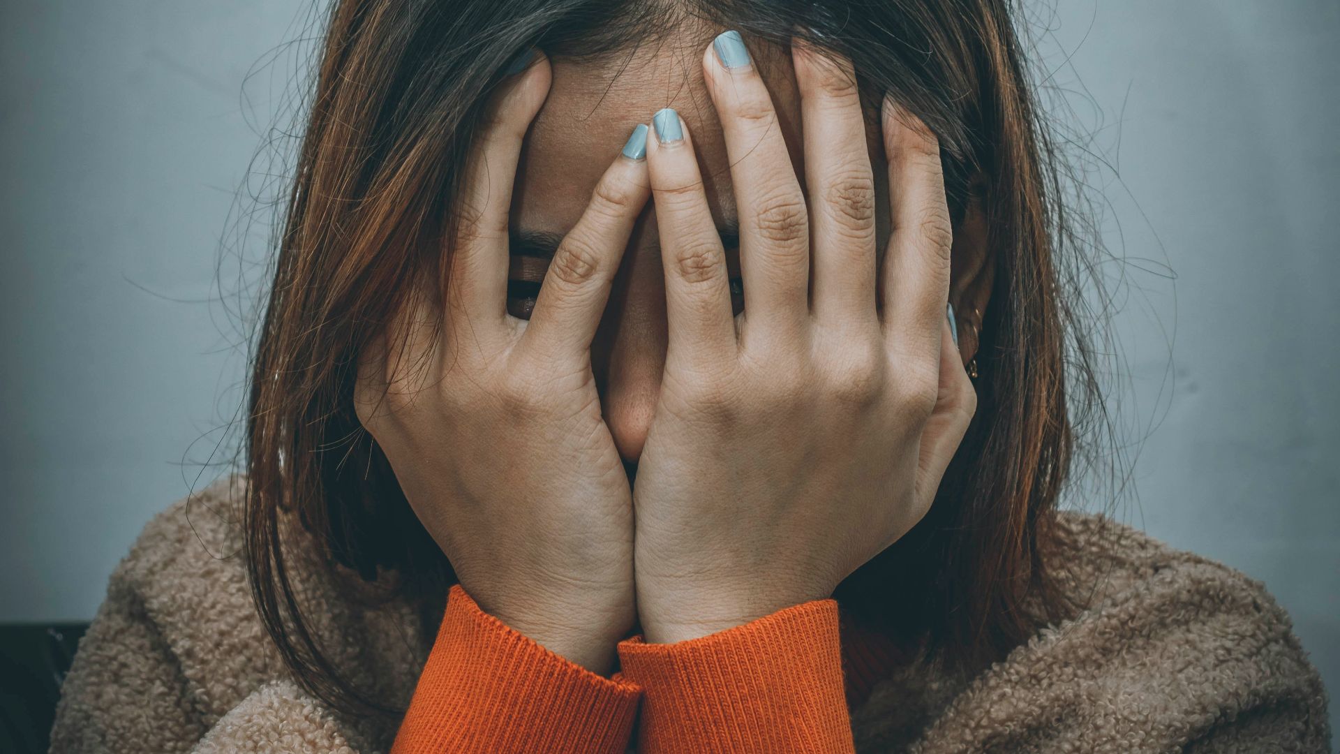 woman in brown sweater covering her face with her hand