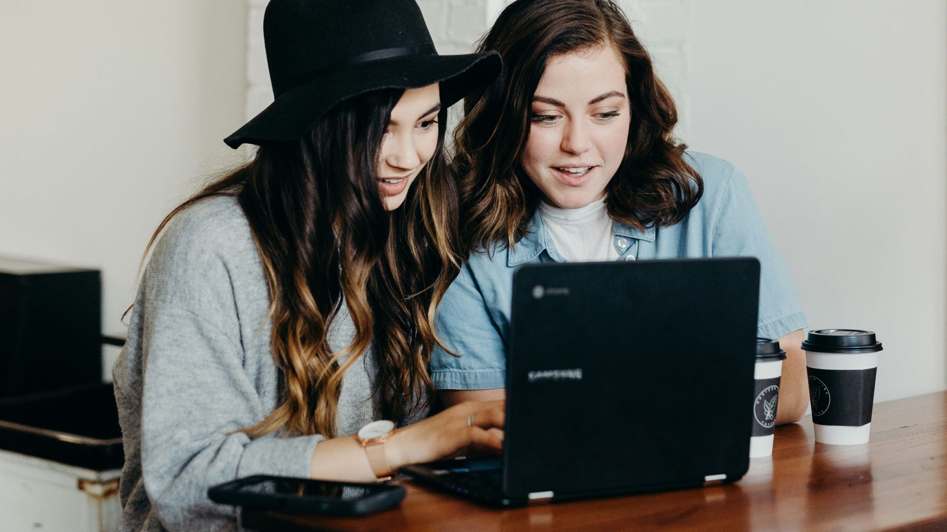 two woman sitting near table using Samsung laptop