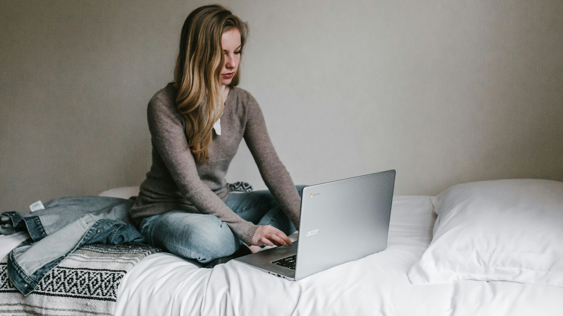 woman typing on MacBook Pro while sitting on bed in room