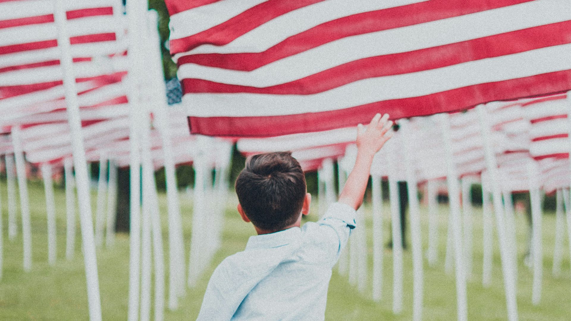 boy in white shirt and blue denim jeans holding us a flag