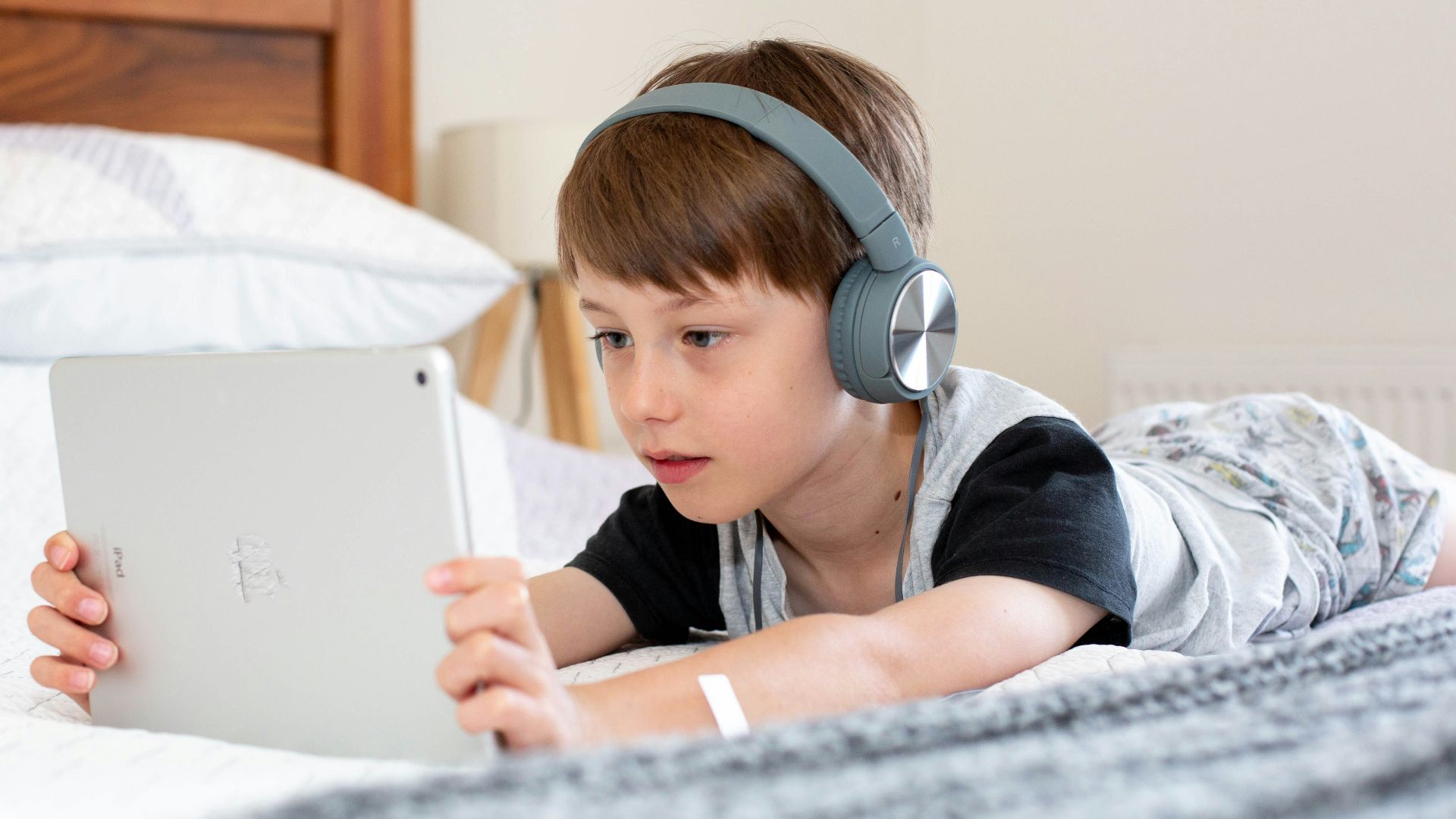 boy in blue shirt wearing headphones lying on bed