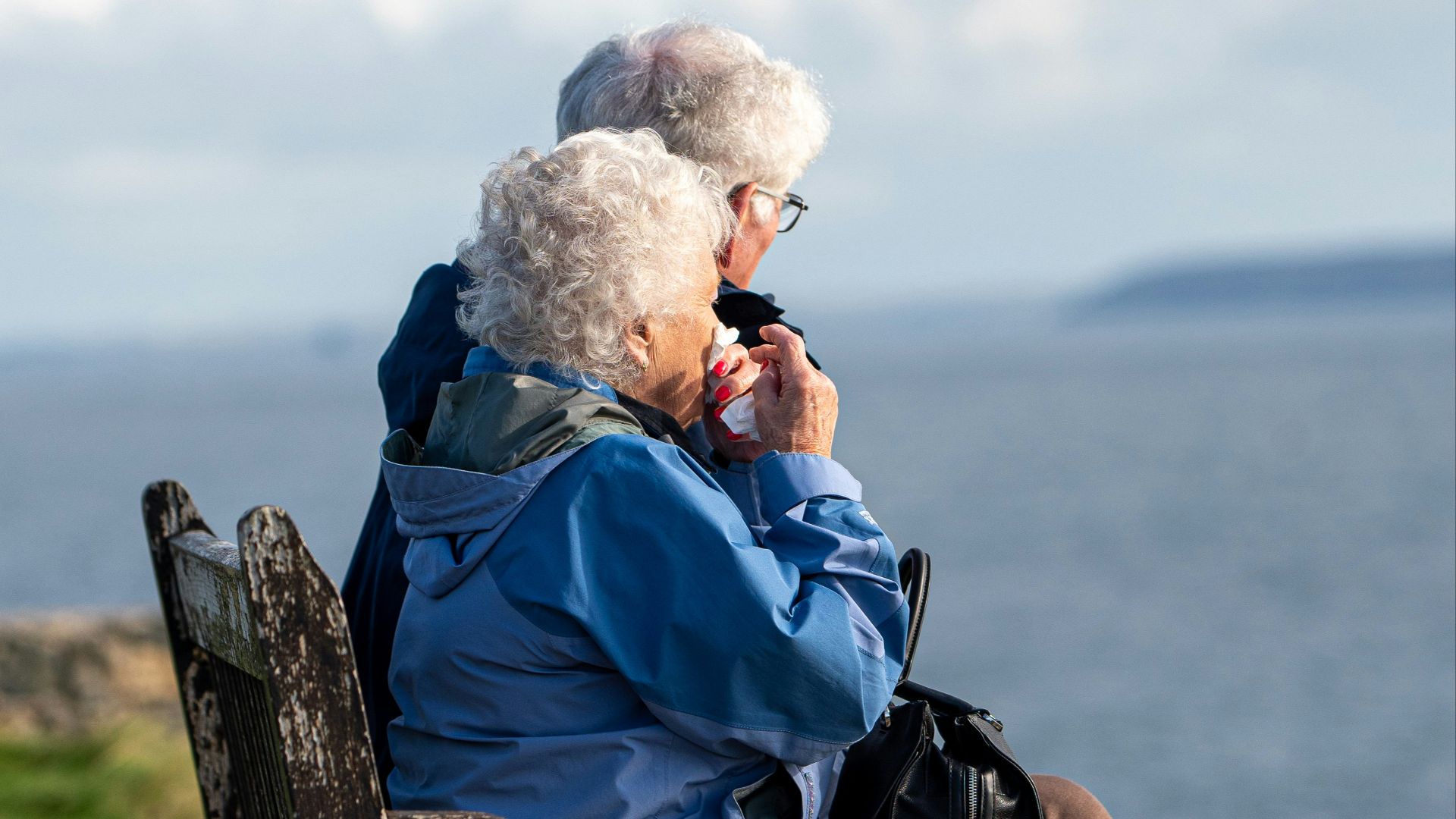 man and woman sitting on gray wooden bench viewing blue sea during daytime