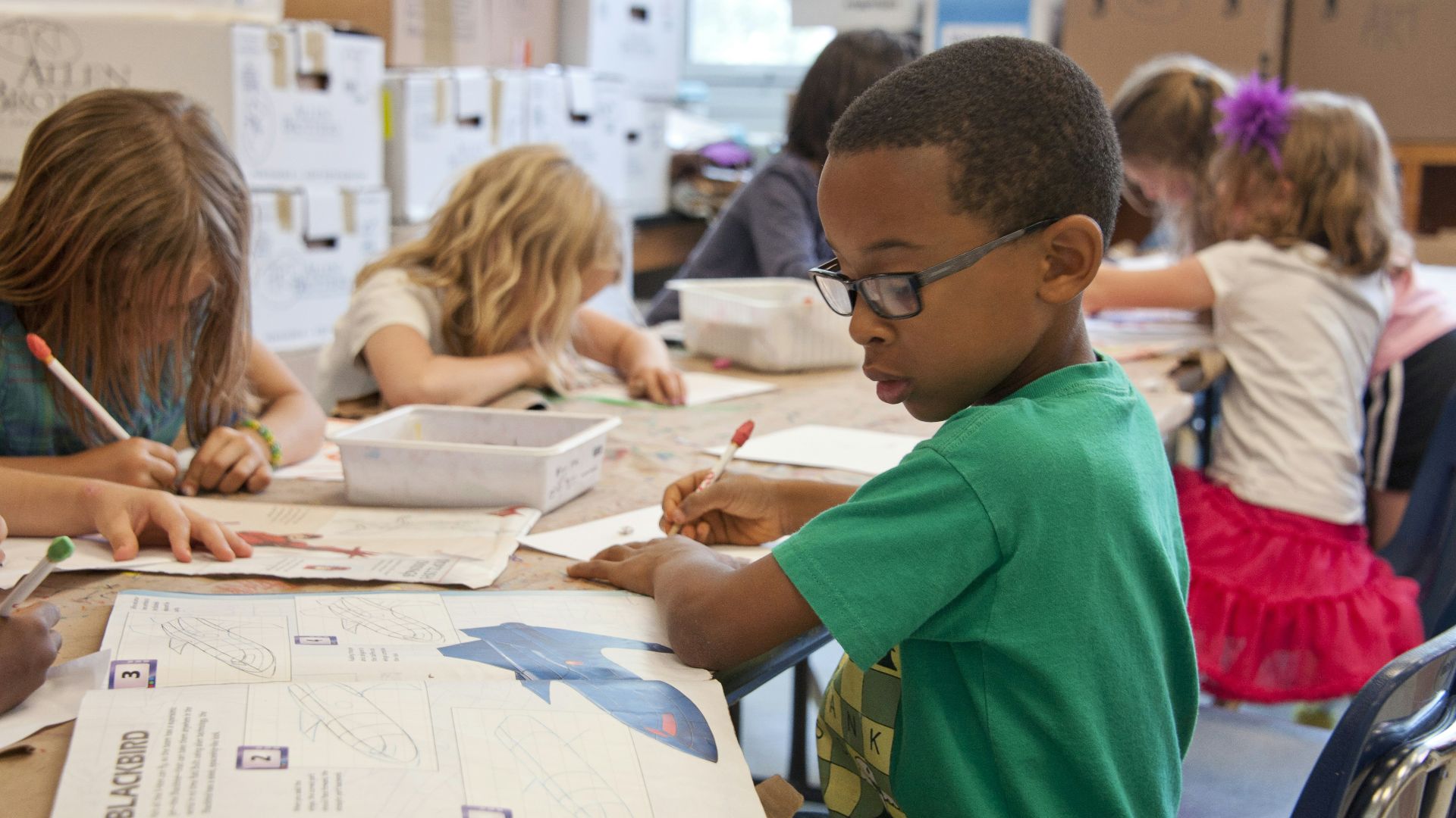 boy in green sweater writing on white paper