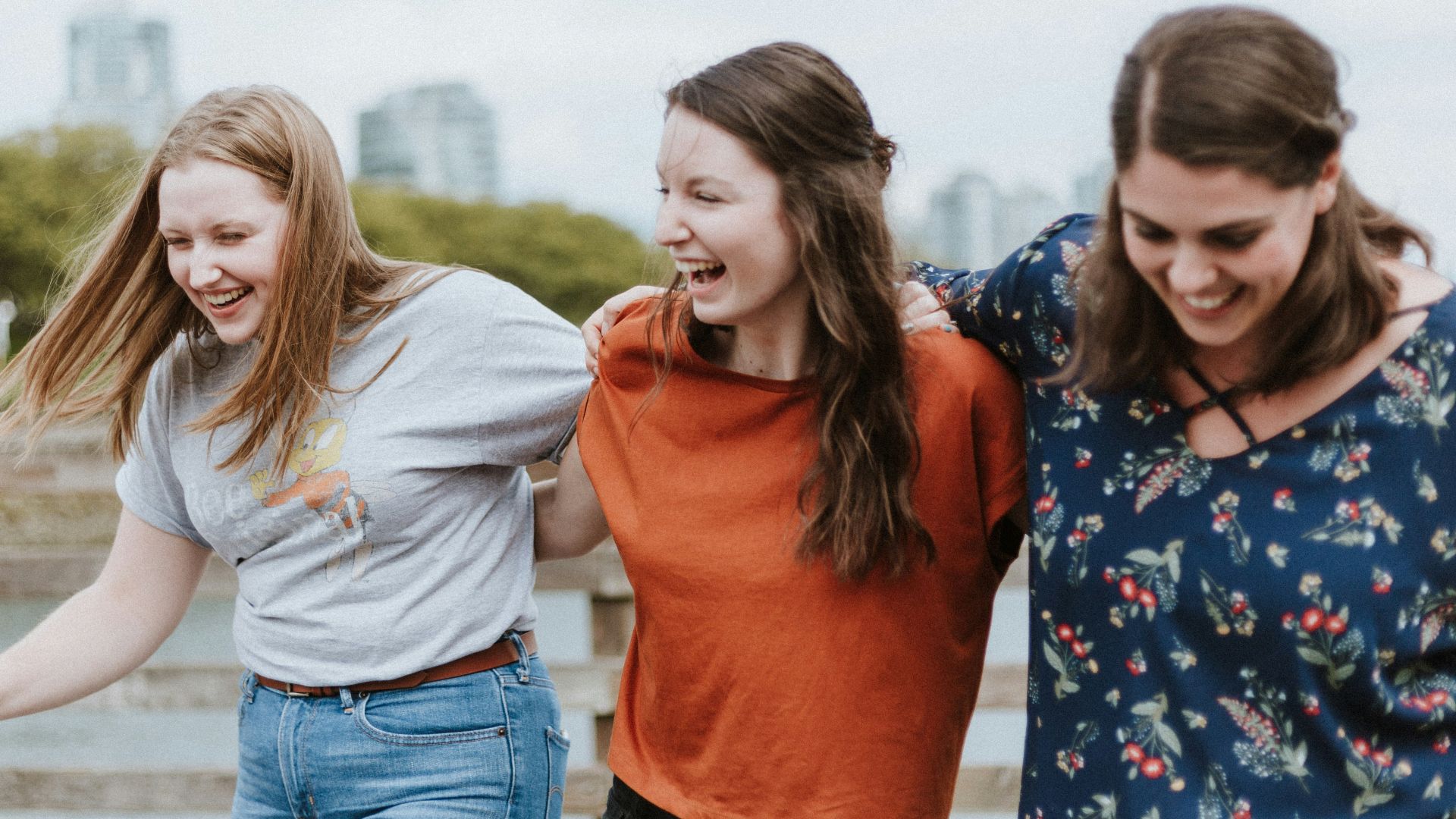 three women walking on brown wooden dock near high rise building during daytime