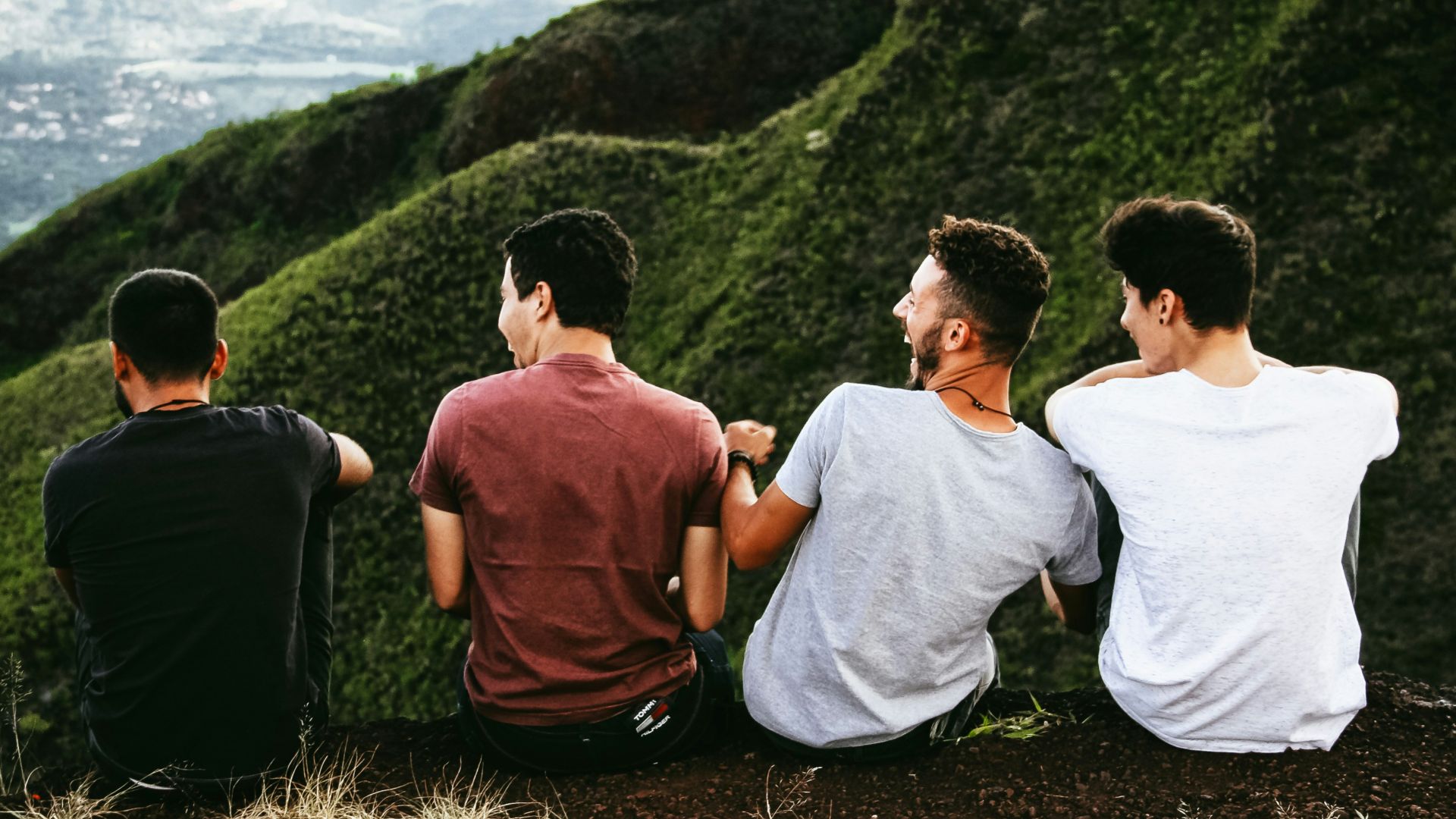 row of four men sitting on mountain trail