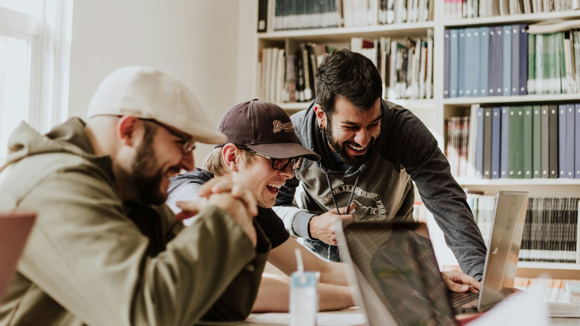 three men laughing while looking in the laptop inside room