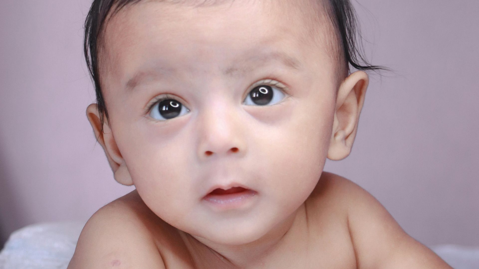topless baby lying on white textile
